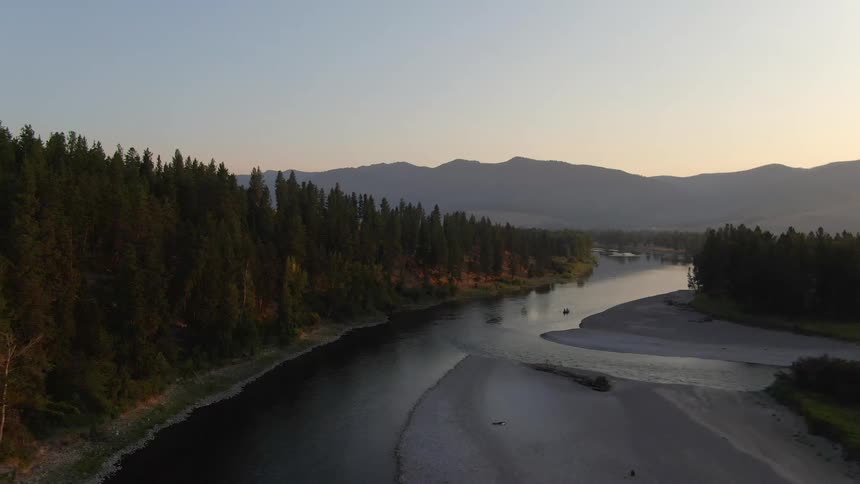 Aerial view of a river through the pine forests near the mountains at sunset