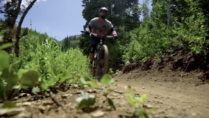 A cyclist with helmet and gloves rides a bicycle down a dirt road in the forest