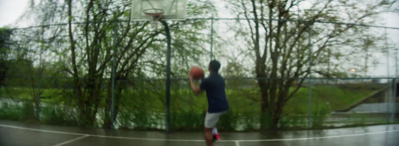 A man performs a layup on a rain drenched outdoors basketball court