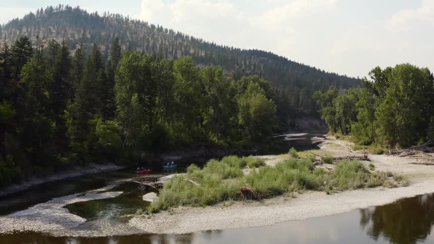 A pair of colorful boats travel down a narrow river between a sandbank and a forest
