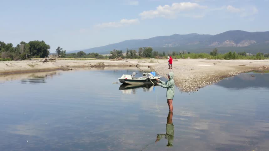 A person stands in a lake and casts a fishing line