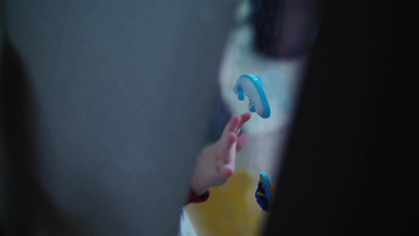 A little boy sticks toys to a window at home