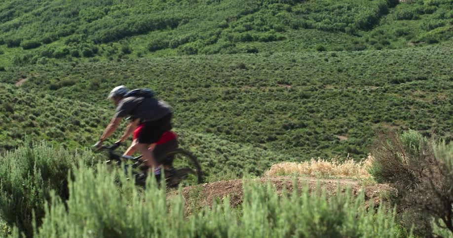 Cyclists drive mountain bikes on a trail through the green hills