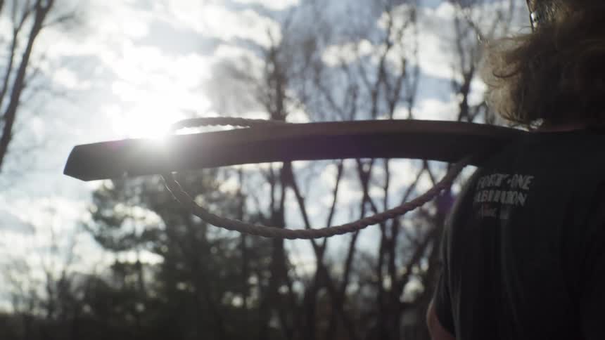 A man walks in the forest with a board connected to a rope