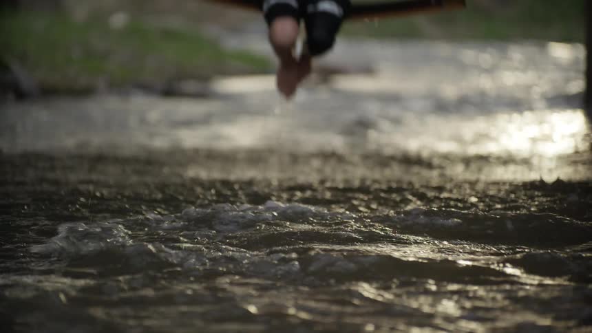 A child using a swing over a stream causing their feet to dip into the stream when the swing nears the ground