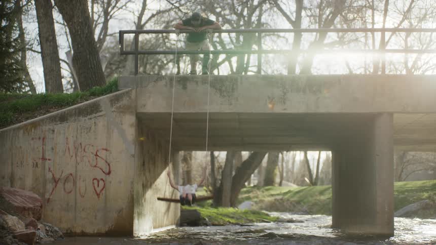 Father swings boy on swing hung on bridge railing over river