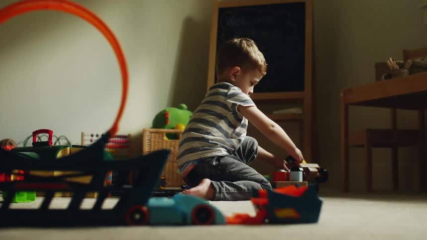 A young boy plays with a toy vehicle on the floor of a play room