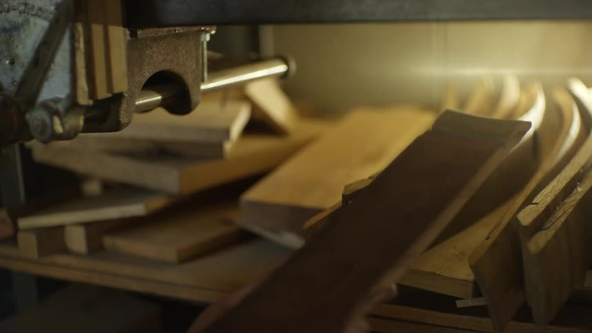 Man in a workshop selects bent wooden planks from a shelf