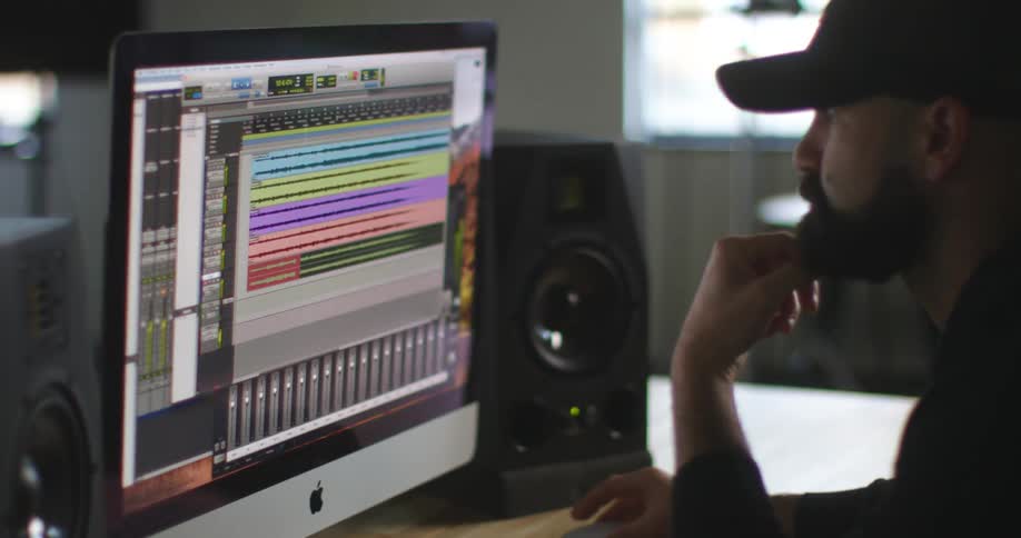 Bearded man wearing a cap looks at graphics on a computer monitor