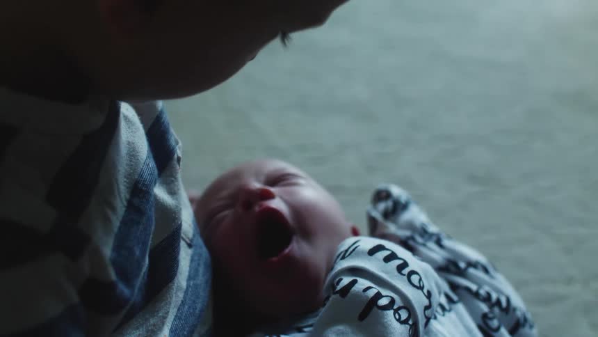 A boy holds and looks down at his yawning infant brother