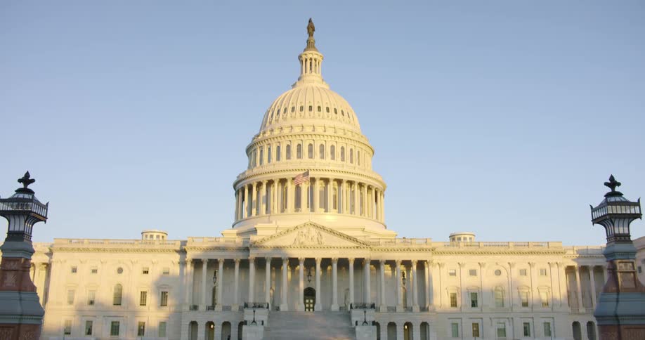 The capital building with american flag in front and the sky and clouds in the background