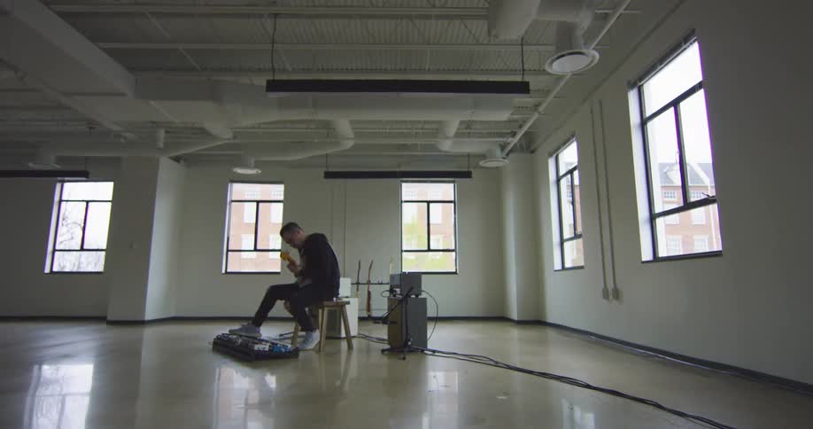A man sitting on a bench playing a guitar with windows in the background