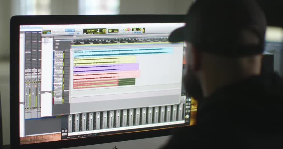 Bearded man wearing a hat looks at graphics on a computer monitor