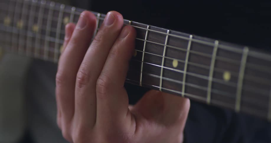 Man wearing a black long sleeve t shirt plays a guitar made of wood with six strings