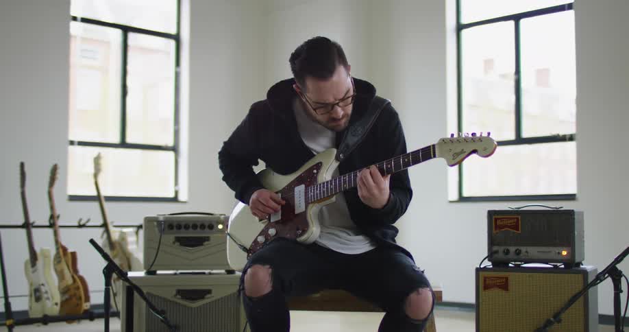 A man sitting on a bench playing a guitar with windows in the background