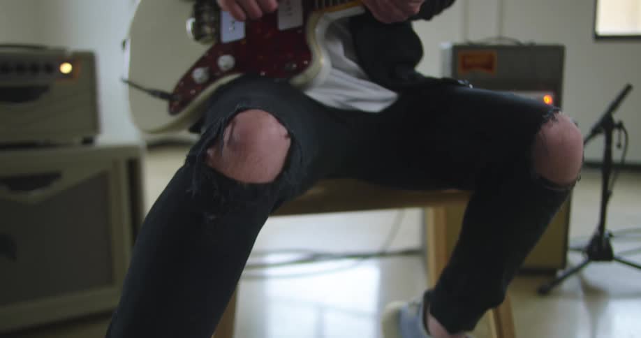 Man sits playing electric guitar and manipulating foot pedal