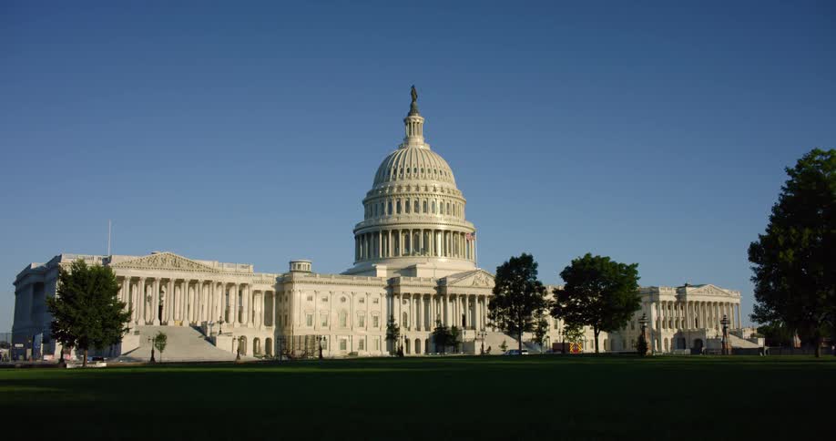 The capital building with grass and trees in the foreground and the sky and clouds in the background