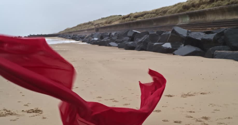 A long red scarf blows in the wind on the beach