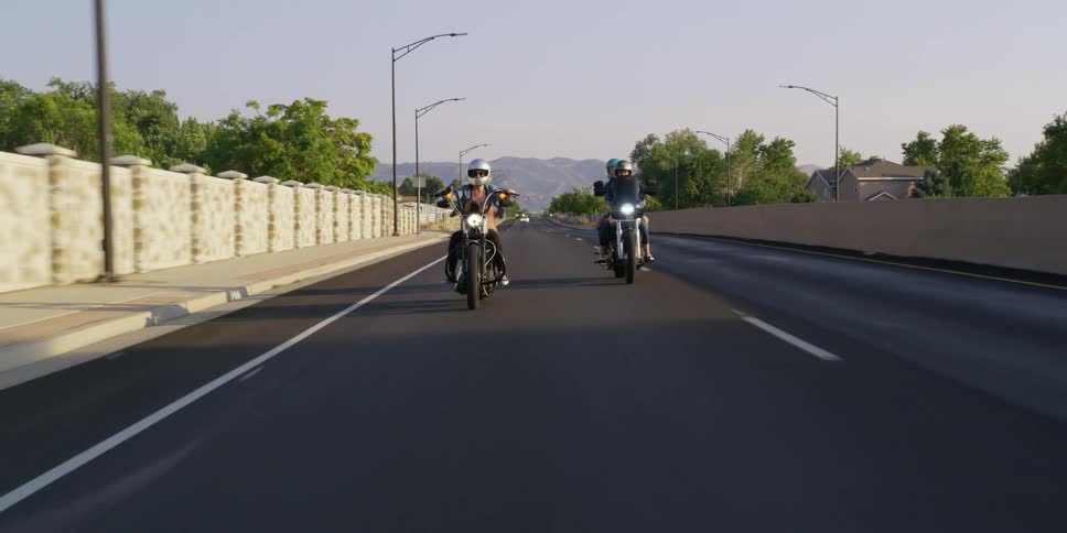 People riding motorcycles down a street in a neighborhood
