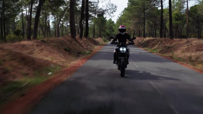 A person wearing a helmet on a motorcycle riding down the road with trees and the sky in the background
