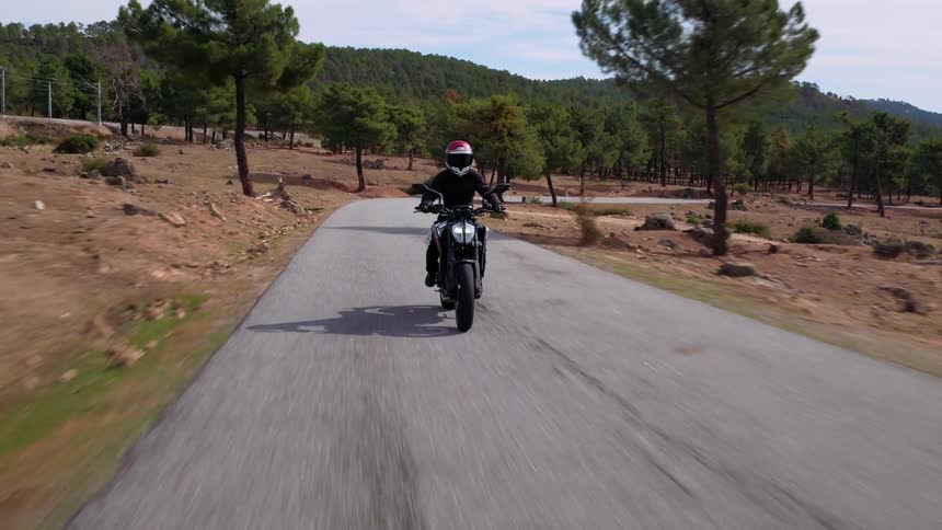 A person with a helmet riding a motorcycle on a road with trees and the sky in the background