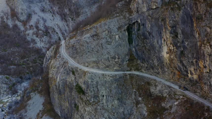 A vehicle drives on a narrow road along a cliff
