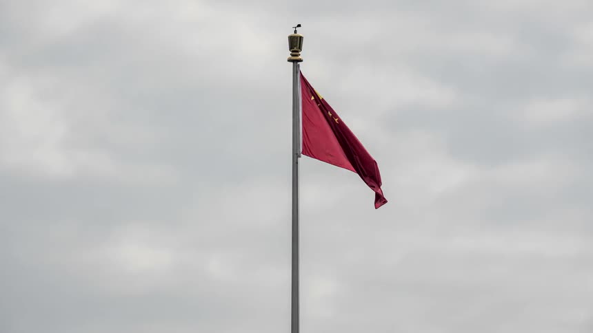 The peoples republic of china flag waving in the wind on a pole with the sky and clouds in the background