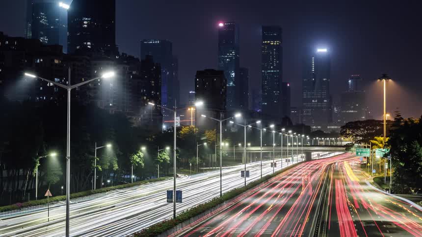 Time lapse of traffic on a highway through the city skyscrapers at night
