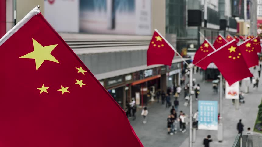 Chinas flags on poles above a city street with people walking and going in and out of stores