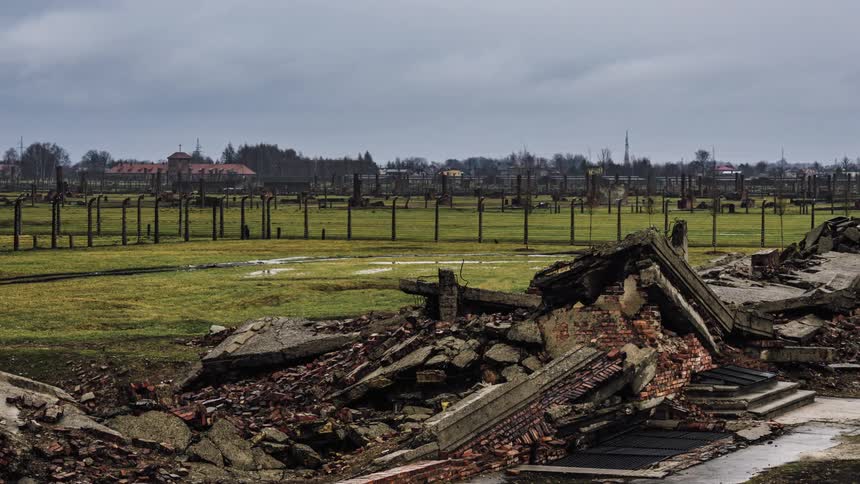 Debris from a burned building sits in a wet field under a cloudy sky