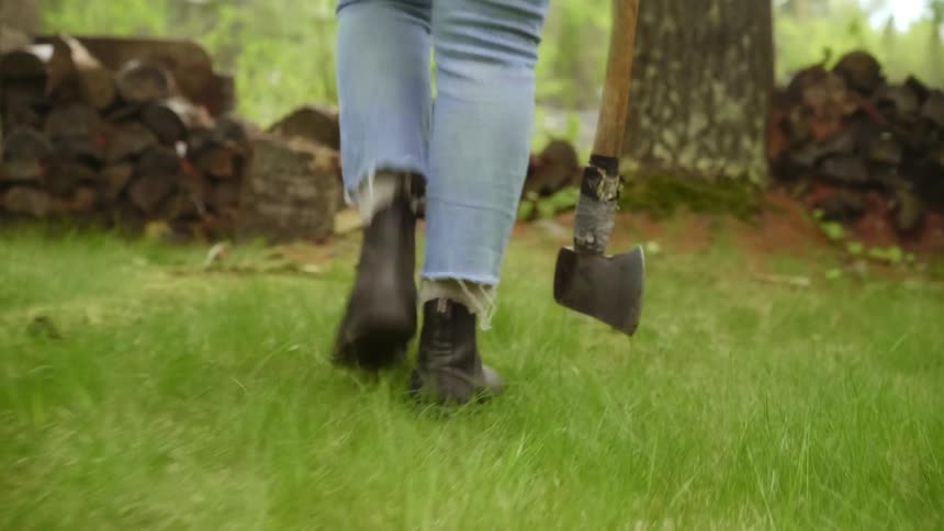 A person walking on grass with an ax with a river and trees in the background