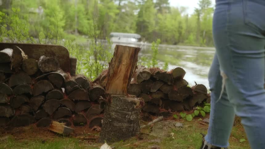 A woman chops wood next to a river