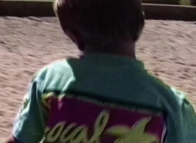 A boy and a girl playing in a park with sand and a slide in the background