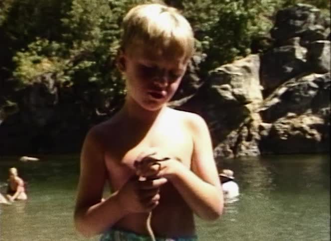 Young boy holds a snake as he stand near a creek