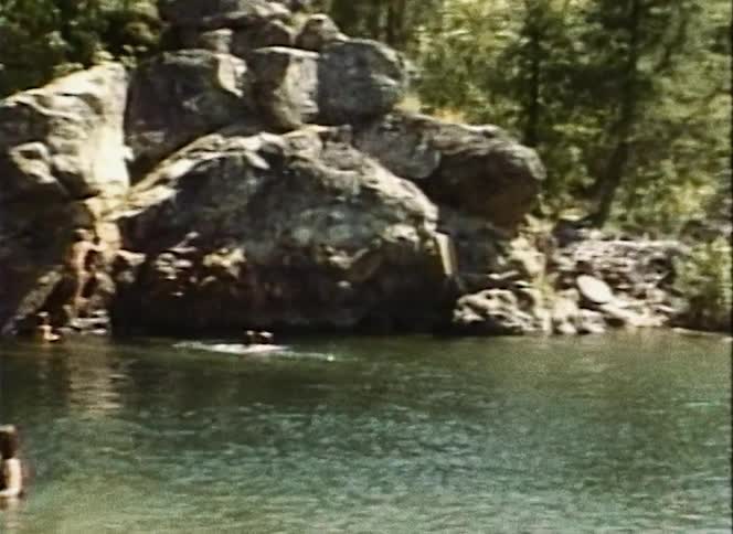 A boy dives off a rock formation into a river where the rest of his family is swimming