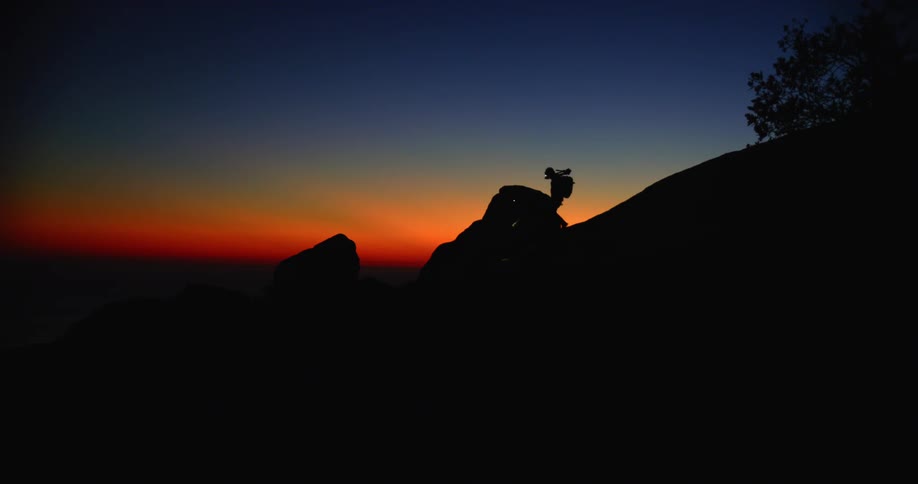 A pair of hikers descend a hill guided by head mounted flashlights just before sunrise