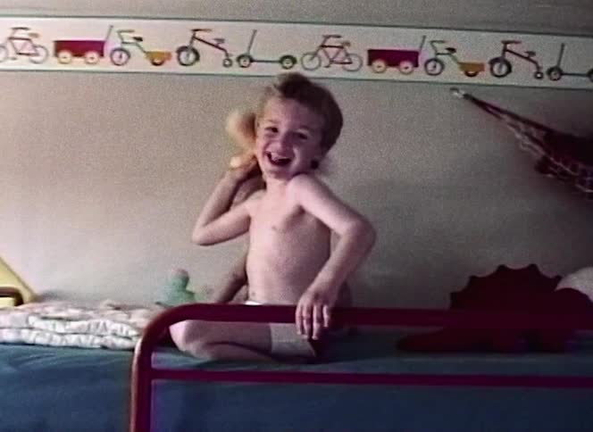 A boy playing on the top of a bunk bed with a younger sibling throws a stuffed animal at the camera