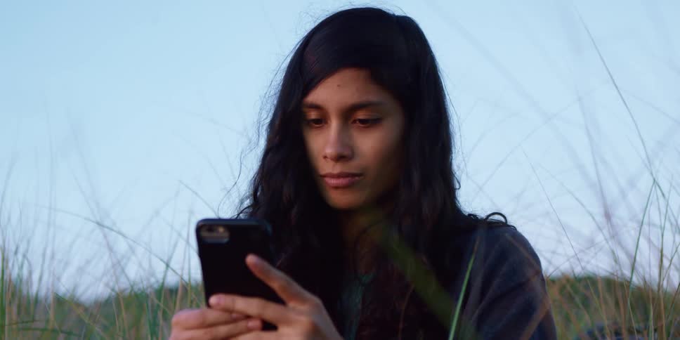 A woman uses her smartphone while sitting in a field