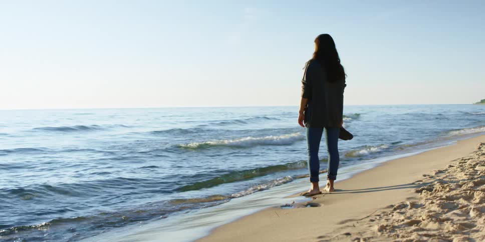 Brunette girl walks barefoot on the beach and watches the sea