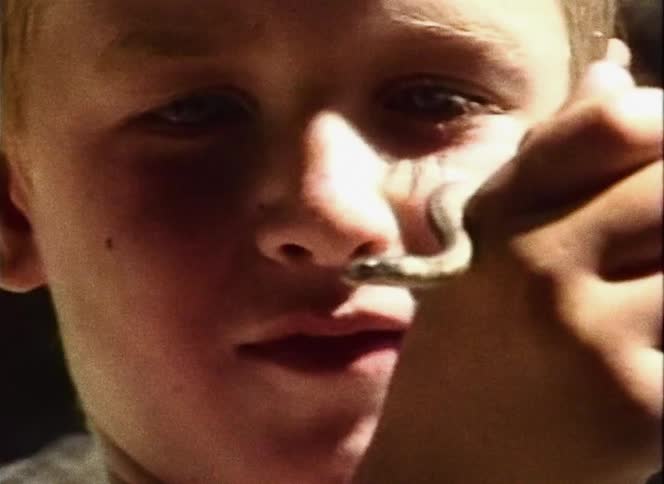Blonde boy standing outdoors holds small snake and talks