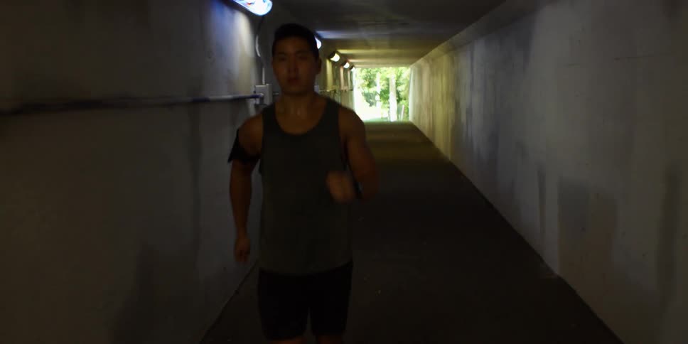 A man jogs through a tunnel that exits to a park