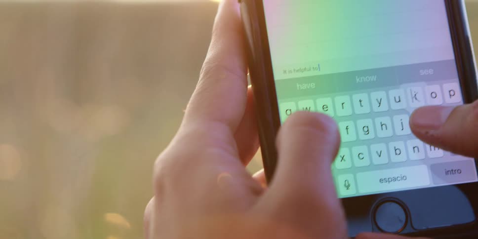 A person types on a smartphone while standing outdoors in a field of tall grass