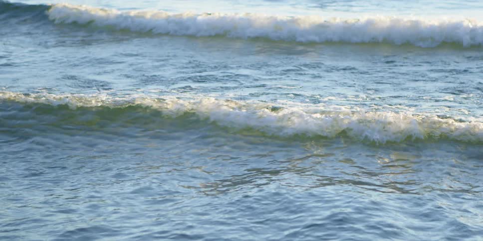 Small waves break against the shore at sunset