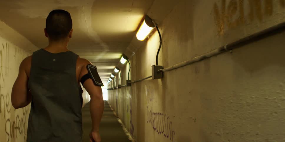 A man in a tank top jobs in a tunnel with graffiti