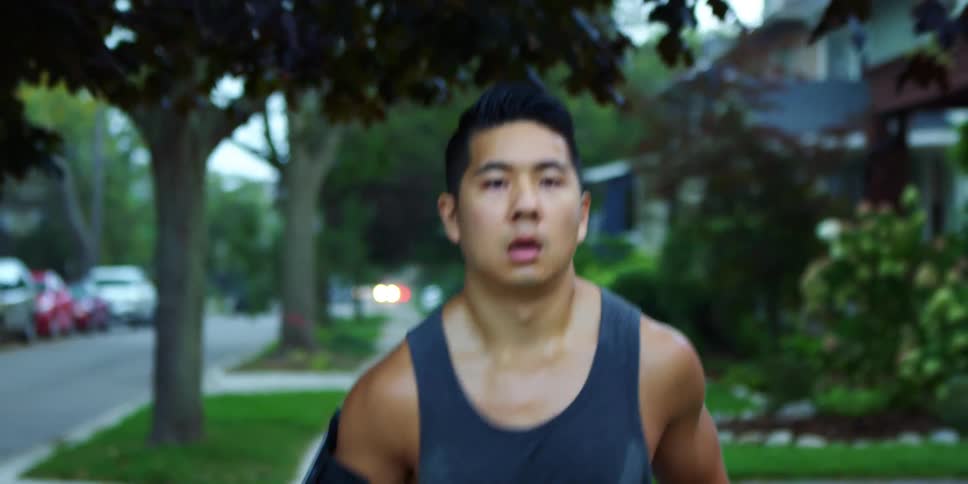 A man running in a neighborhood with trees and houses in the background