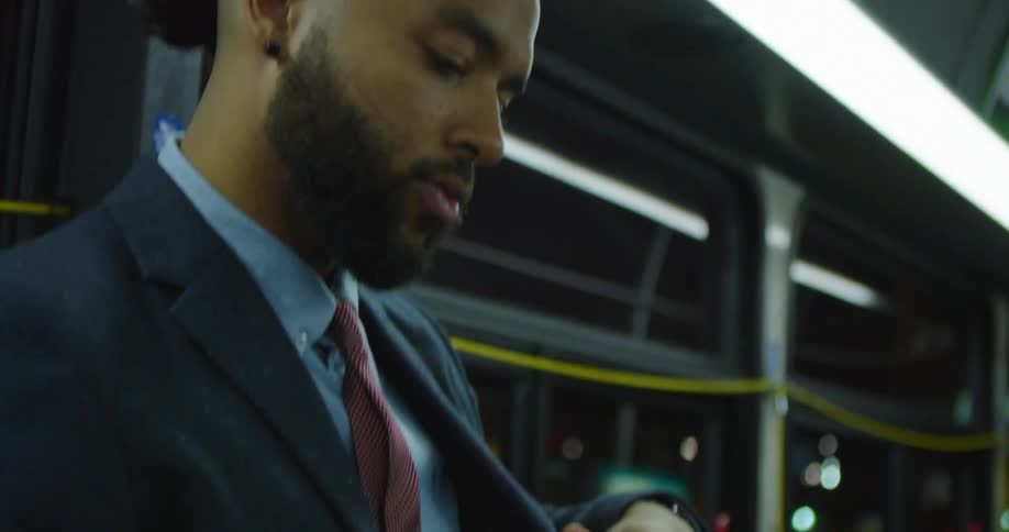 A man in a business suit checks his phone while riding public transportation