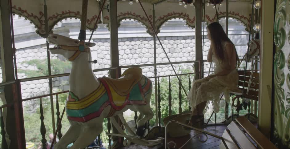 A woman is riding a merry go round wearing a white dress