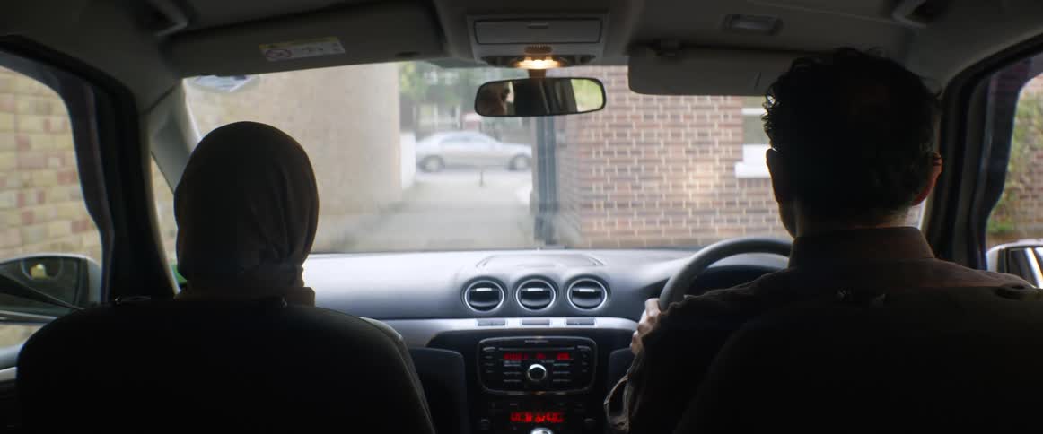 A man and a woman sitting in a car in the back of an alley