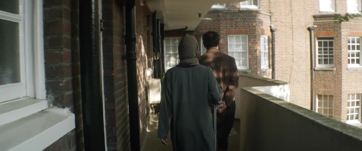 In a foreign nation a woman walks behind a man on a balcony