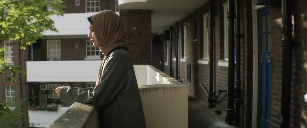 Brunette woman with a brown headscarf stands on the balcony